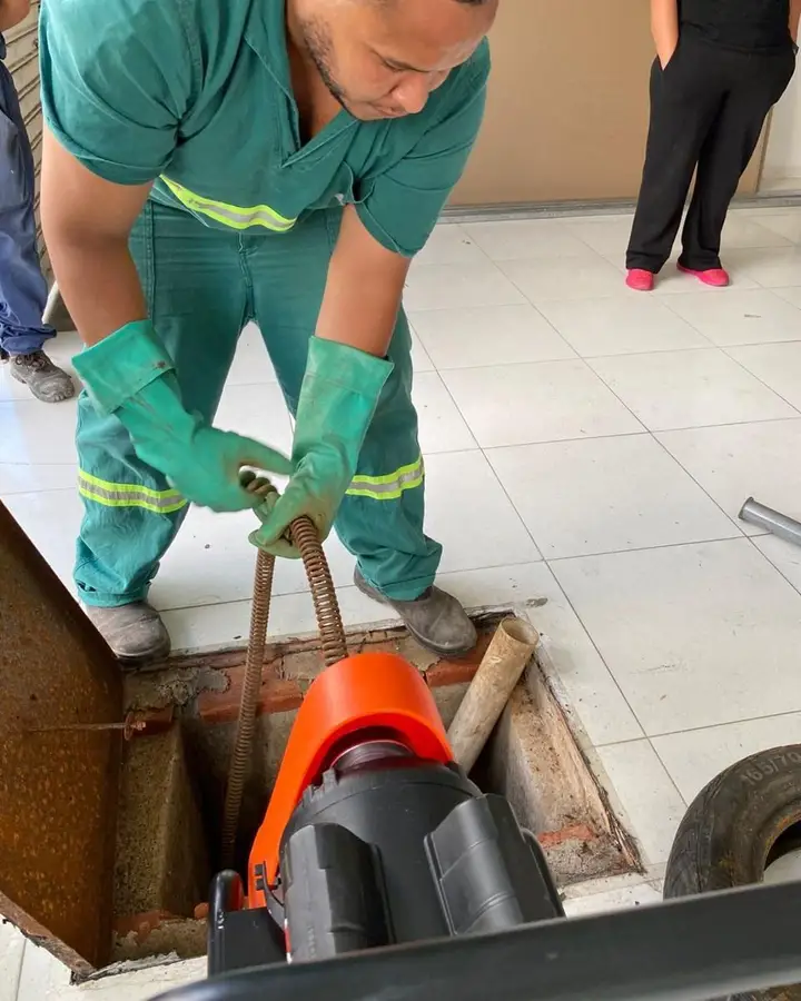 Profissional da FS Desentupimento desobstruindo caixa de esgoto com máquina rotativa